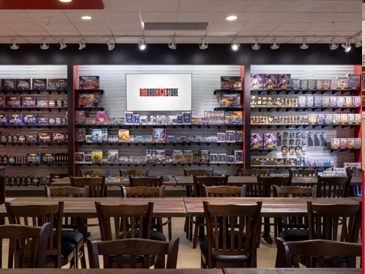 Retail showroom and gaming area for BigBadGameStore, featuring open shelving with inventory and tables for daily customer play.