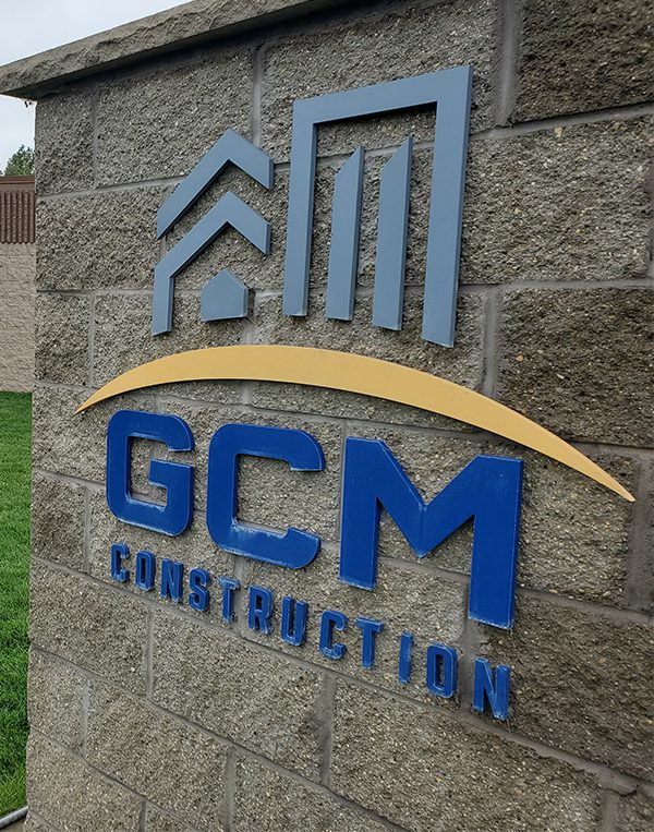 Close-up of the GCM Construction company sign mounted on a textured gray stone wall.