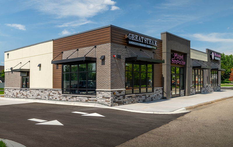Exterior of a Great Steak and Planet Smoothie franchise location in Blaine, Minnesota, featuring modern stonework, large windows, and a paved parking lot.