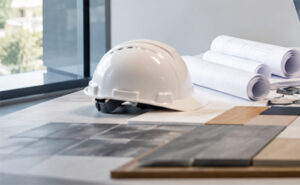 A construction hard hat and rolled-up architectural blueprints resting on a desk, representing the planning and consultation phase of a commercial construction project.