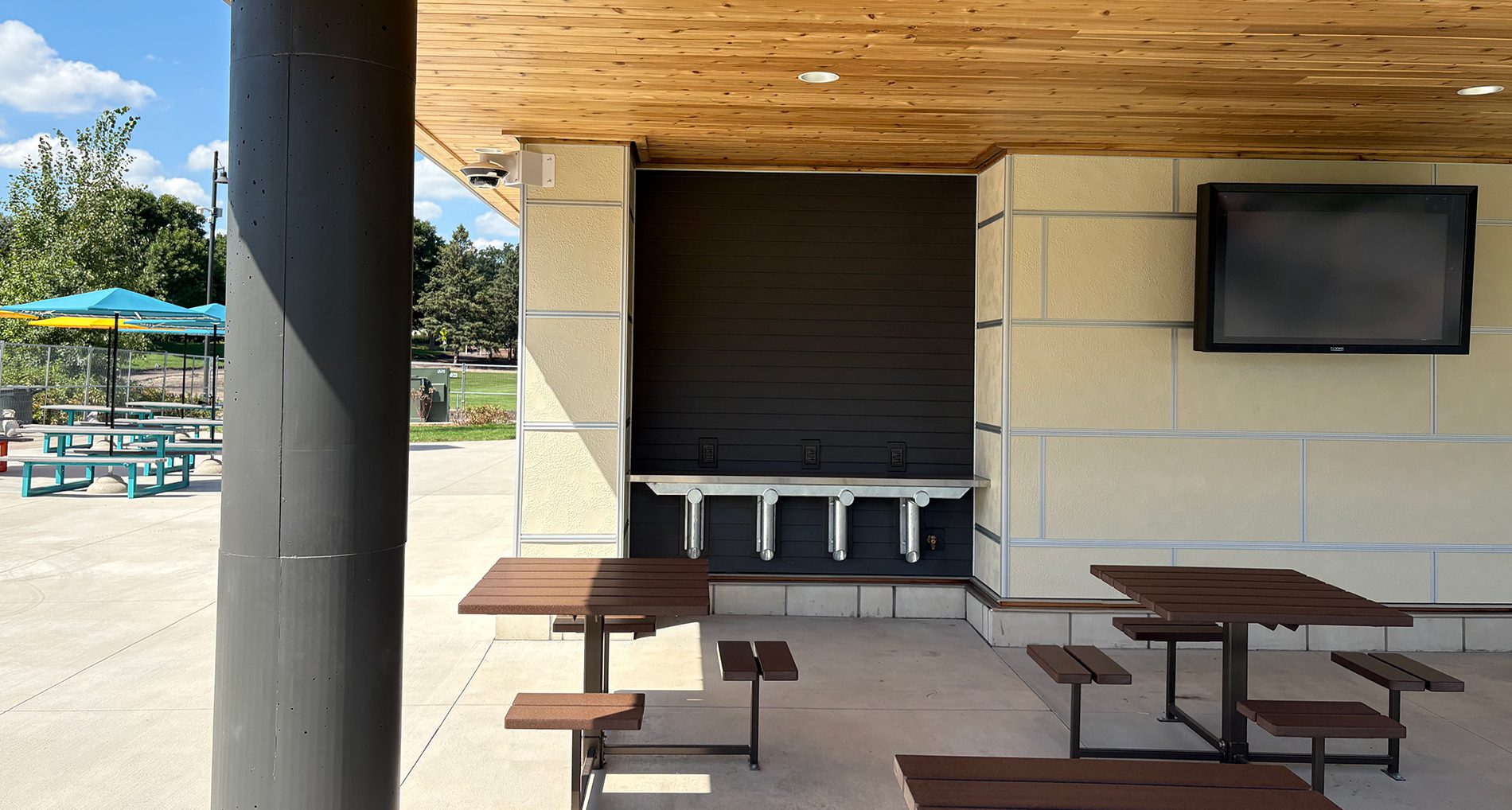 Covered outdoor pavilion at the Shoreview Commons municipal park, featuring heavy timber framing, concrete seating, and a large paved plaza.