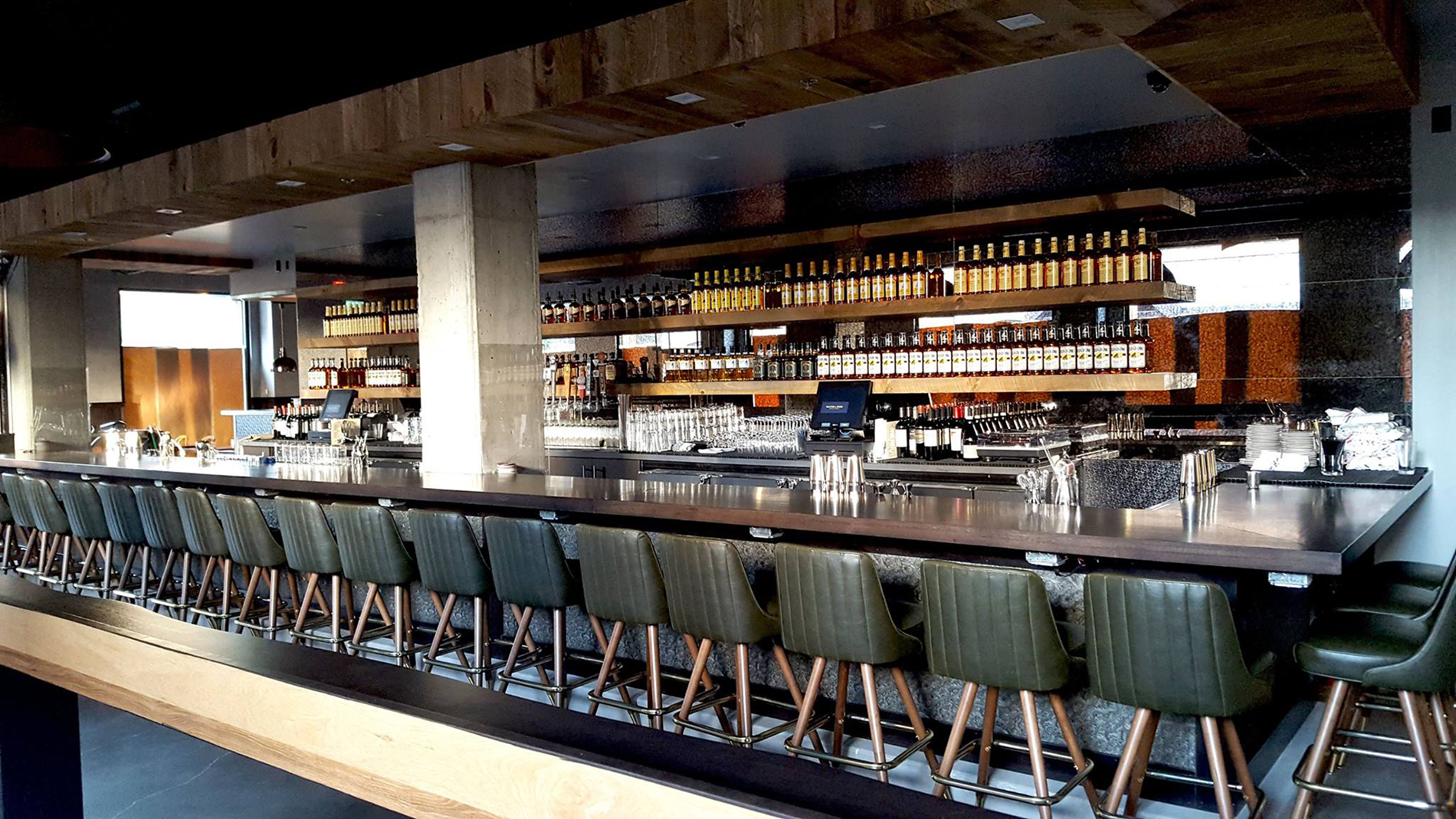 Modern restaurant bar interior in Minneapolis, featuring polished wood countertops, green leather bar stools, and warm ambient lighting.
