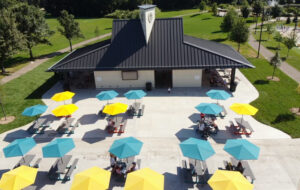 Aerial view of the Shoreview Commons park pavilion in Shoreview, Minnesota, featuring a covered seating area with colorful patio umbrellas, tables, and surrounding green space.
