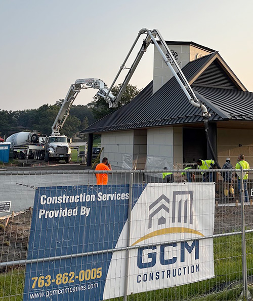 GCM Construction company sign mounted on a gray stone wall, identifying the contractor at a project site.