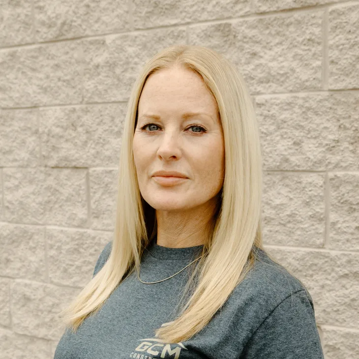 Alana B., Administrative Specialist at GCM Construction, wearing a collared shirt in front of a concrete block wall.