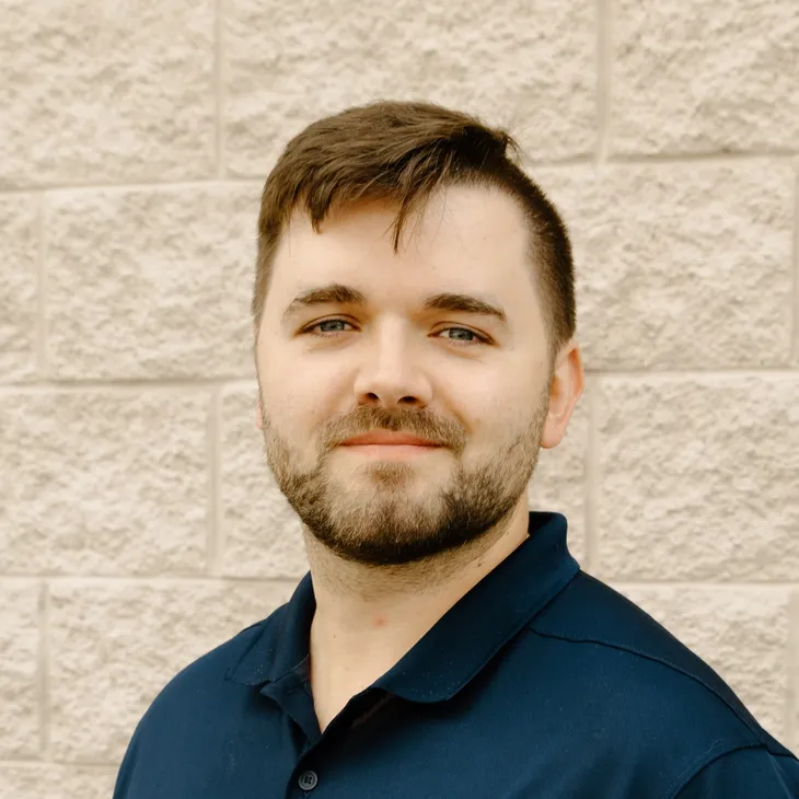 Blake B., Director of Sales & Marketing at GCM Construction, wearing a collared shirt in front of a concrete block wall.