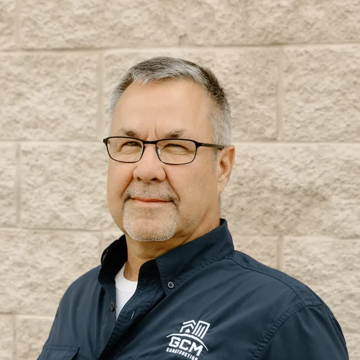 Doug S., Operations Manager at GCM Construction, wearing a collared shirt in front of a concrete block wall.