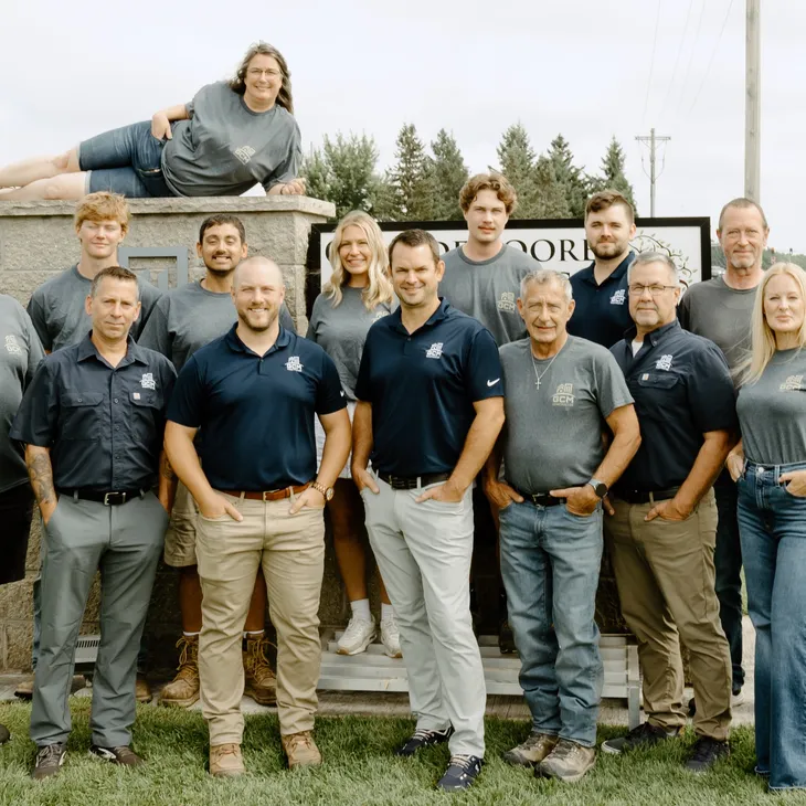 Group photo of the GCM Construction team in Blaine, Minnesota, standing outside in front of a brick wall.
