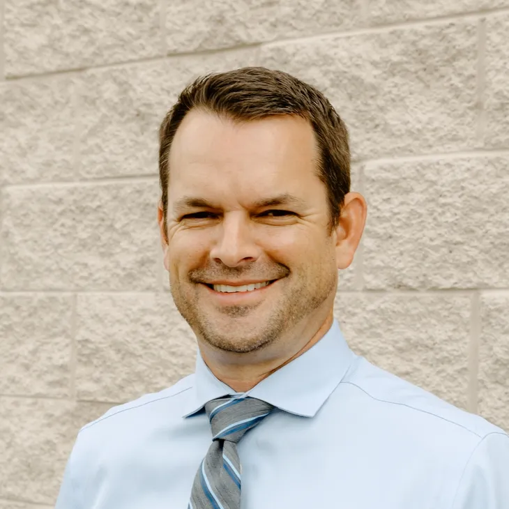 Greg Austin, President at GCM Construction, wearing a collared shirt in front of a concrete block wall.