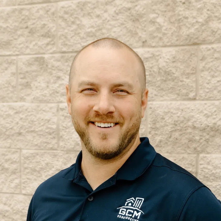 Kyle B., project manager at GCM Construction, wearing a collared shirt in front of a concrete block wall.