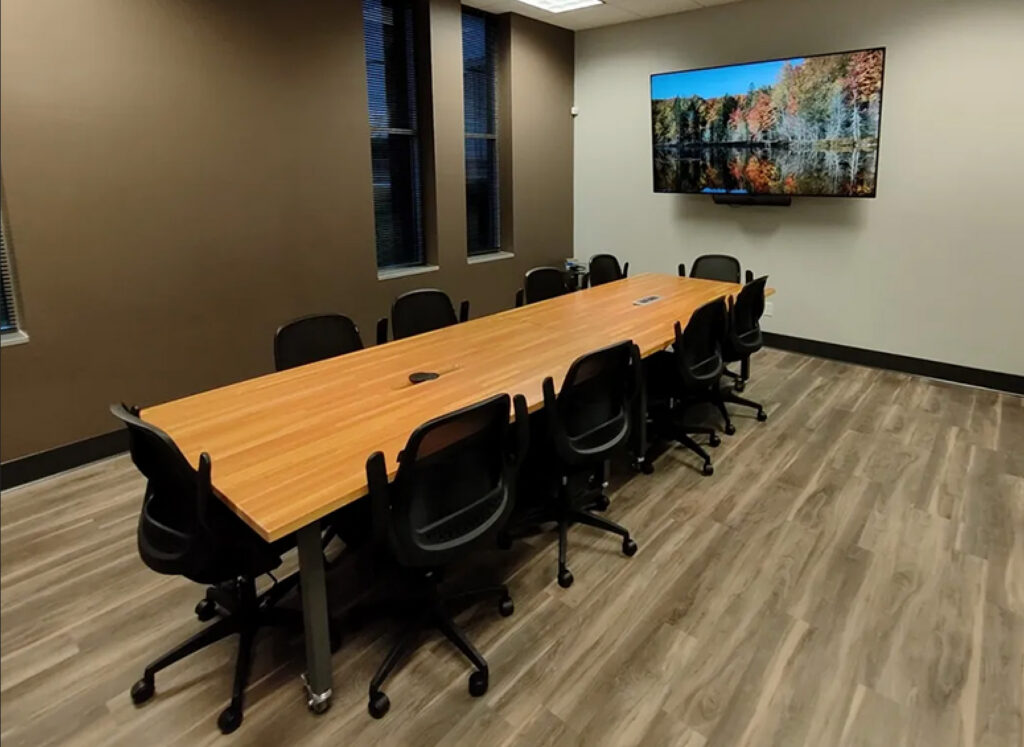 Modern office conference room featuring a large, polished wood table surrounded by comfortable chairs, highlighting a professional office buildout by GCM Construction.