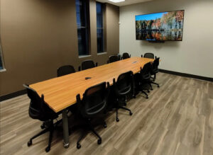Modern office conference room featuring a large, polished wood table surrounded by comfortable chairs, highlighting a professional office buildout by GCM Construction.
