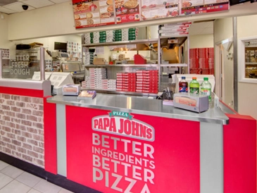 Interior of a Papa John's franchise restaurant featuring a service counter, pizza preparation area, and branded signage.