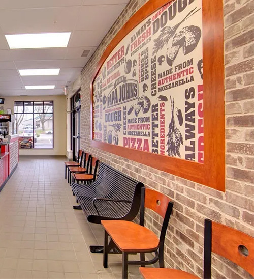 Interior of the Papa John’s restaurant in Maple Grove, Minnesota, showing the customer dining area with wall-mounted branding, highlighting a commercial buildout by GCM Construction.