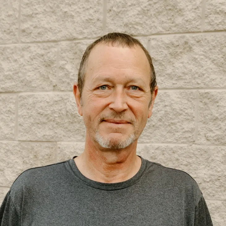 Russ V., senior estimator at GCM Construction, wearing a collared shirt in front of a concrete block wall.